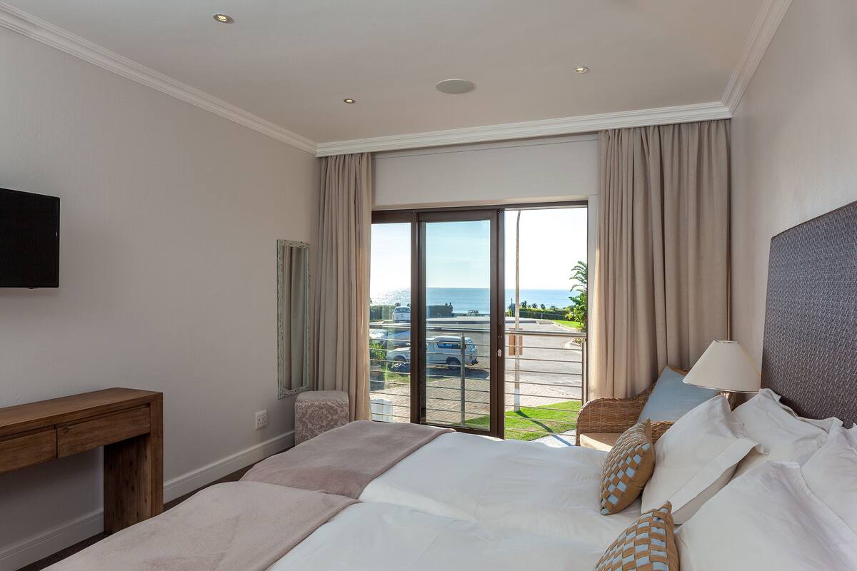 Ein Hotelzimmer mit einem großen Bett, einem Nachttisch aus Holz, einem an der Wand montierten Fernseher und Meerblick durch eine Glastür.