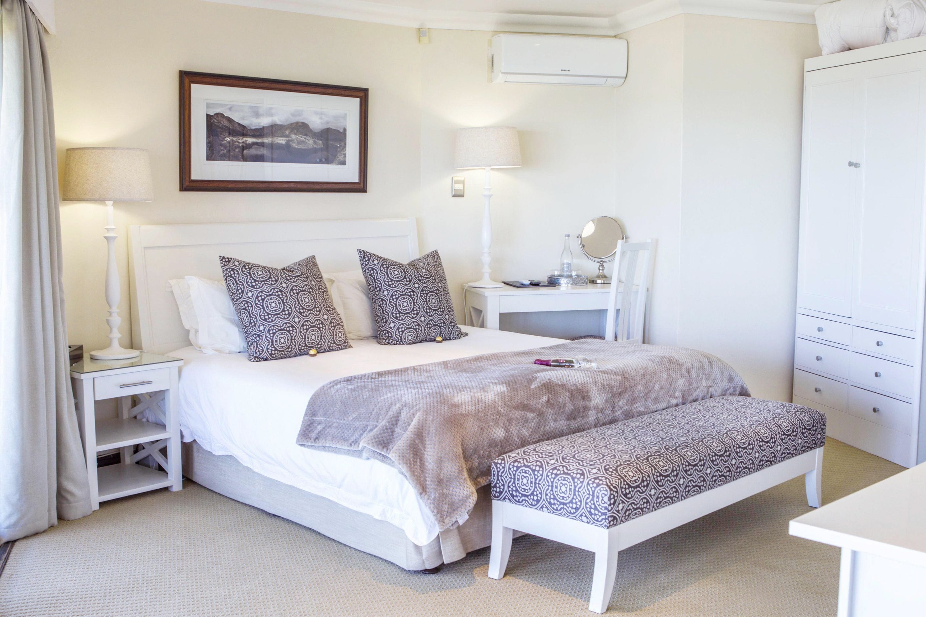 A neatly arranged bedroom with a bed, bedside tables, a bench, a mirror, and a wardrobe.