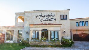 A building with the sign "Shiptubes Collection" on the facade, featuring a large arched entrance, multiple windows, and a gravel driveway. - Super Tubes Guesthouse (Jeffreys Bay)