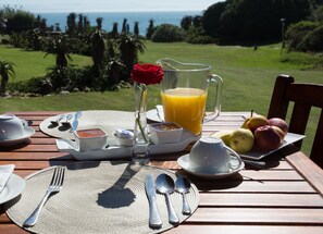 Una mesa de desayuno servida con una jarra de jugo de naranja, una rosa en un vaso y un plato de fruta.