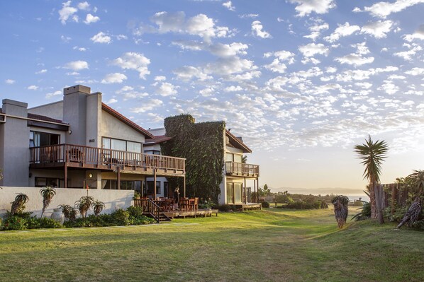 A modern two-story house with a balcony, a well-maintained lawn, and a clear sky. - Super Tubes Guesthouse (Jeffreys Bay)
