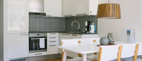 A modern kitchen with white cabinetry, a built-in oven, a stainless steel range hood, and a wooden dining table with chairs.