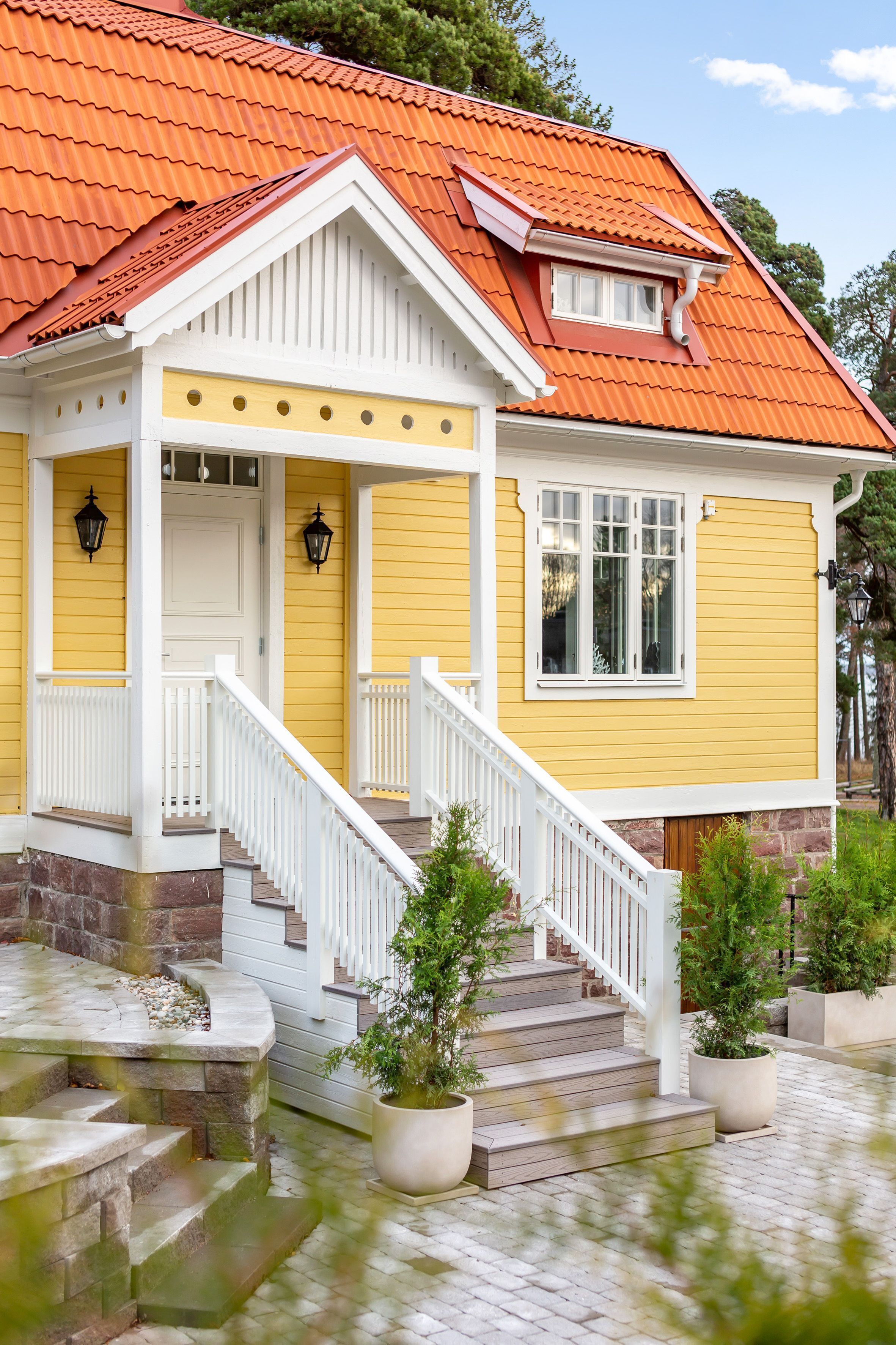 A yellow house with a red roof, white trim, and a front porch with steps.
