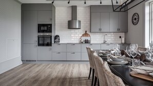 A modern kitchen with grey cabinets, a stainless steel range hood, and a dining area with a table set for four. - Engeltofta Sea Lodge Hotel (Gävle)
