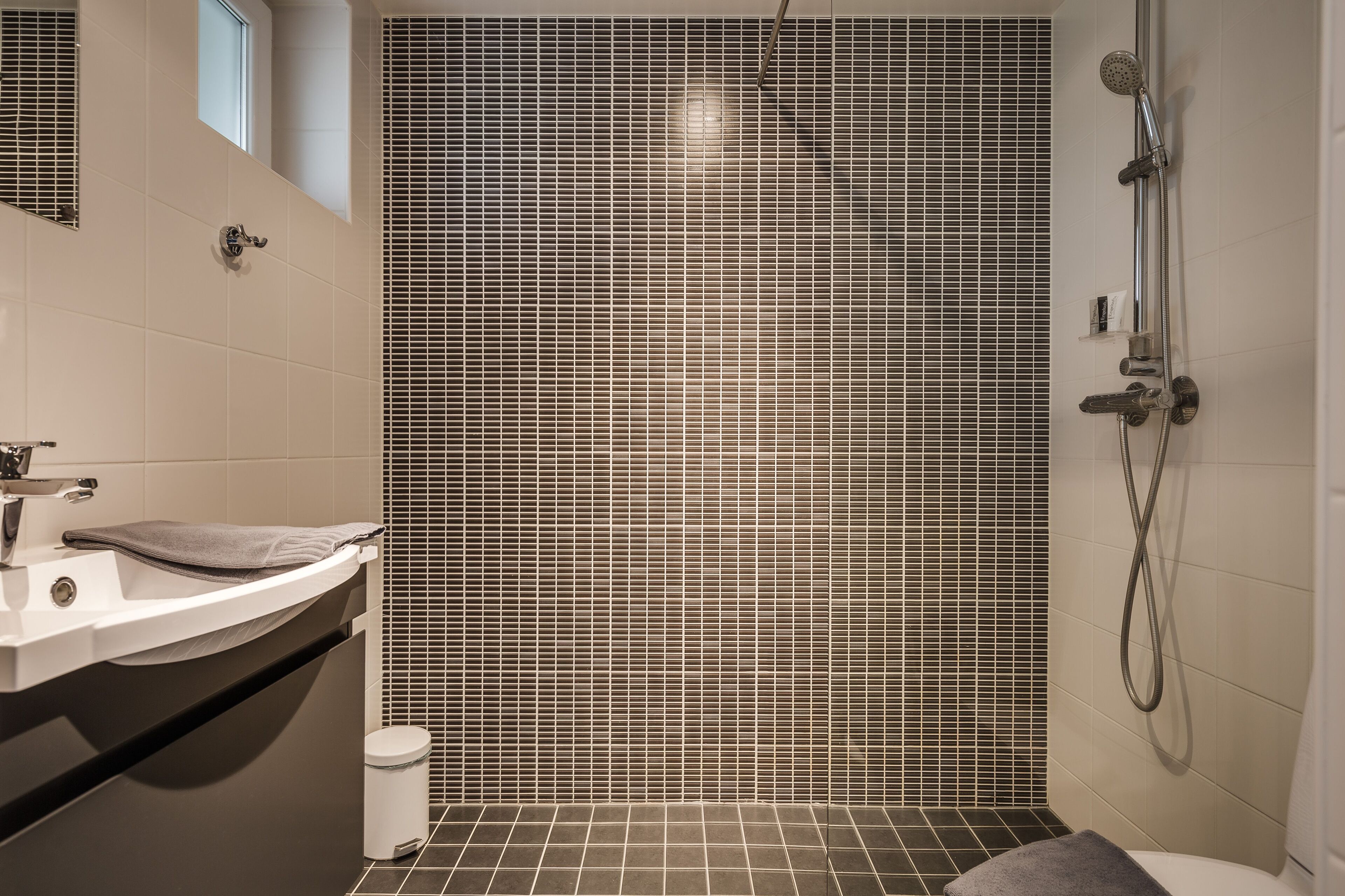 Un baño moderno con cabina de ducha azulejada, un lavabo con una toalla y un inodoro.