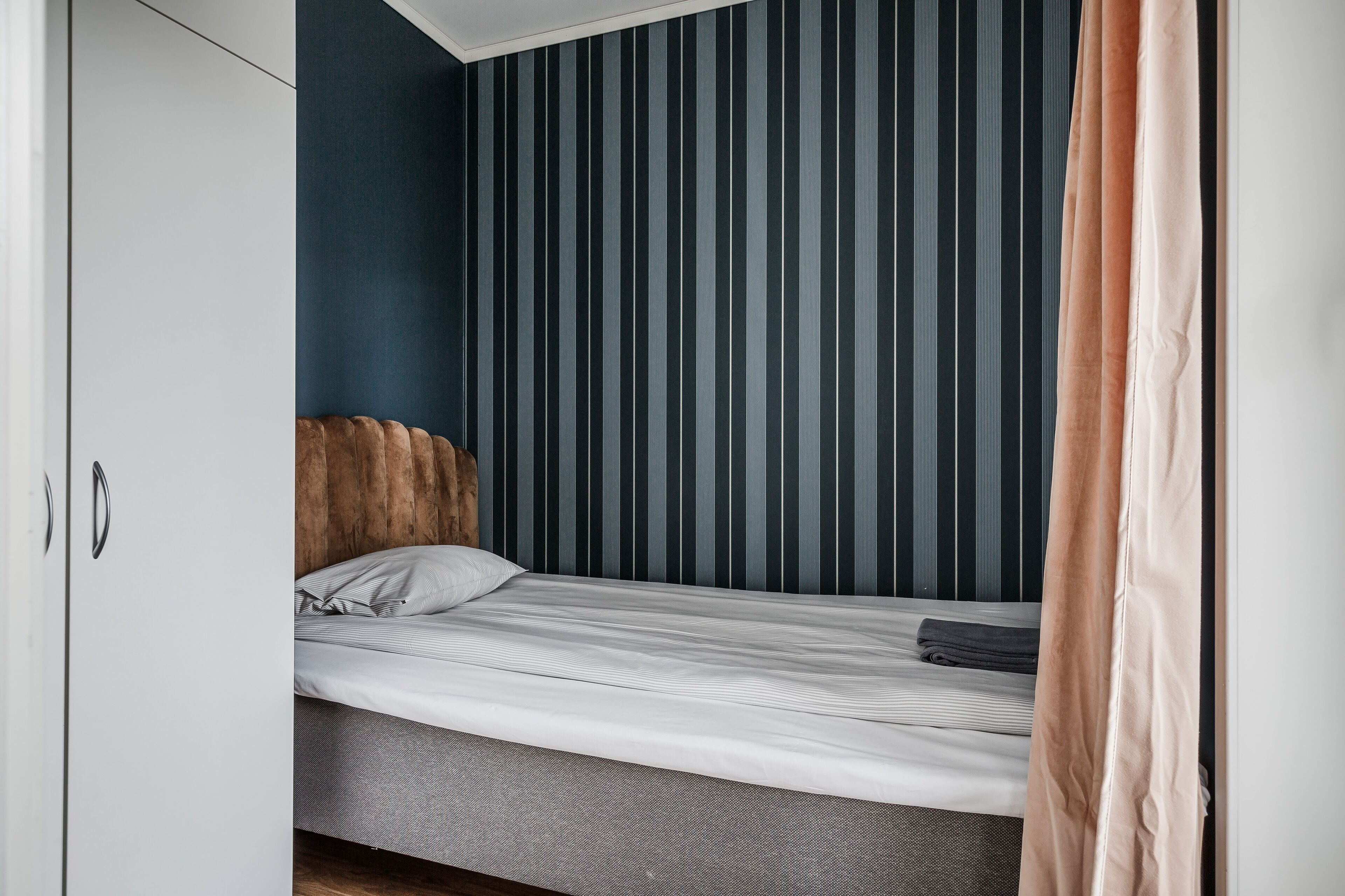 Un dormitorio con cama, armario y pared a rayas.