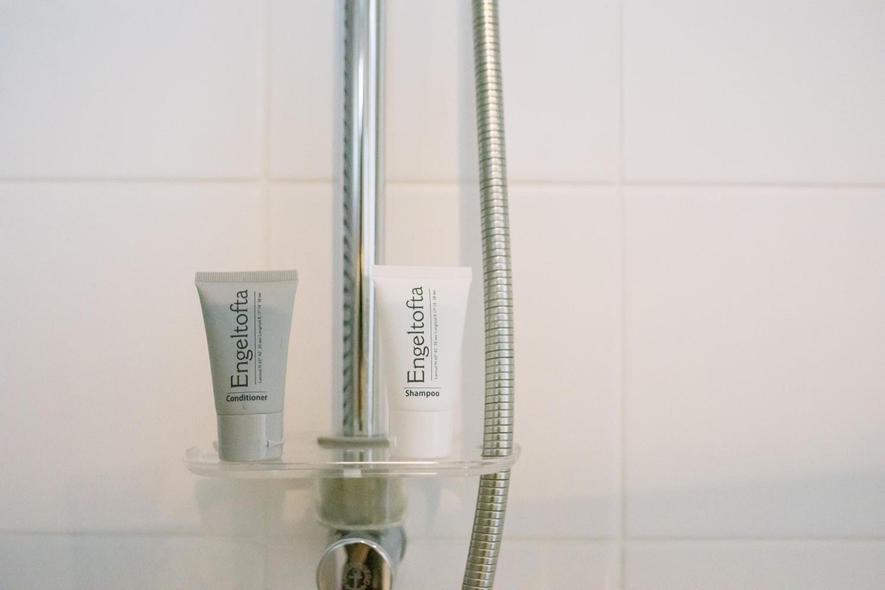 Un baño con cabezal de ducha, plato de ducha de vidrio y dos productos Engeltofta: acondicionador y champú.