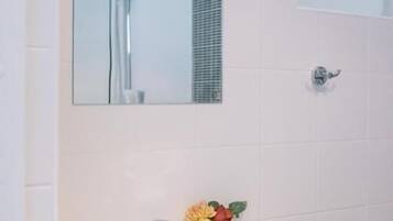 Une salle de bain avec un lavabo blanc, un miroir, une douche et une petite fenêtre.