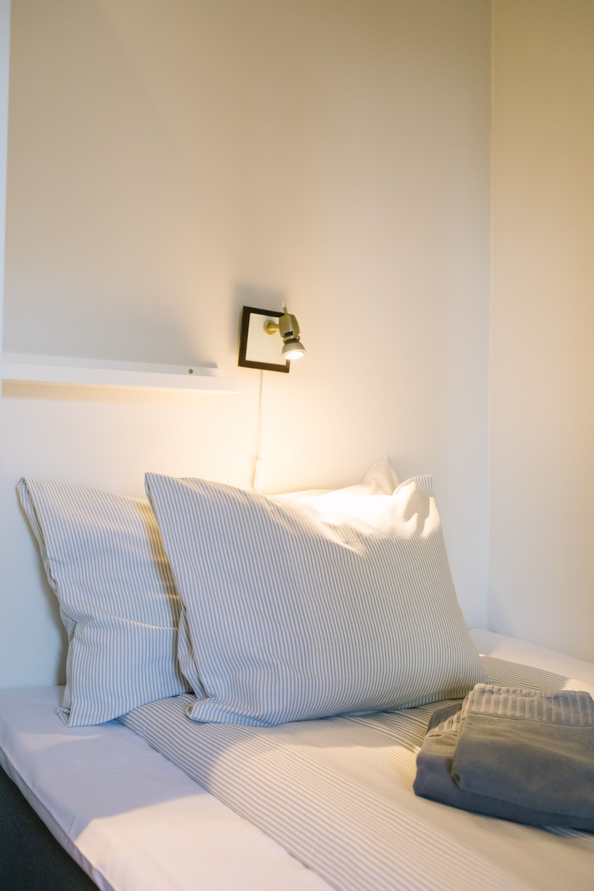 A neatly made bed with striped bedding and a folded gray blanket.