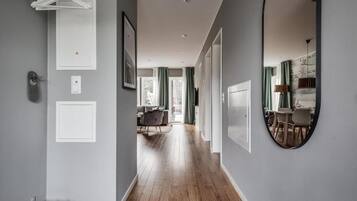 Un pasillo con piso de madera, una puerta blanca y un espejo que refleja un comedor con sillas y una mesa.