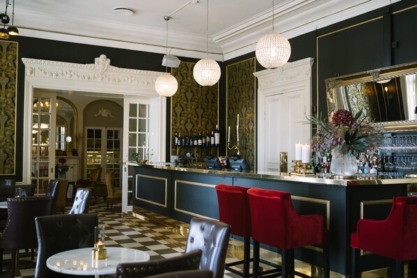 A bar area with a checkered floor, red bar stools, and a bar counter with a mirror and various bottles. - Engeltofta Sea Lodge Hotel (Gävle)