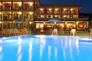 Un hotel con piscina, area relax esterna e facciata ben illuminata.