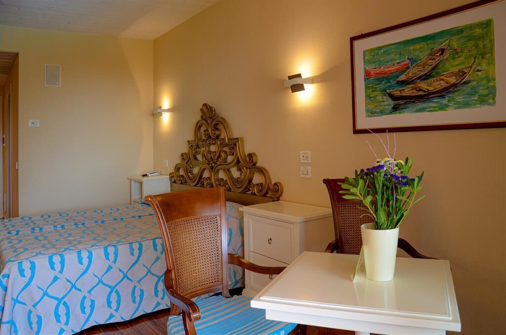 A bedroom with a bed, a nightstand, a dresser, a chair, a table, and a wall-mounted lamp.