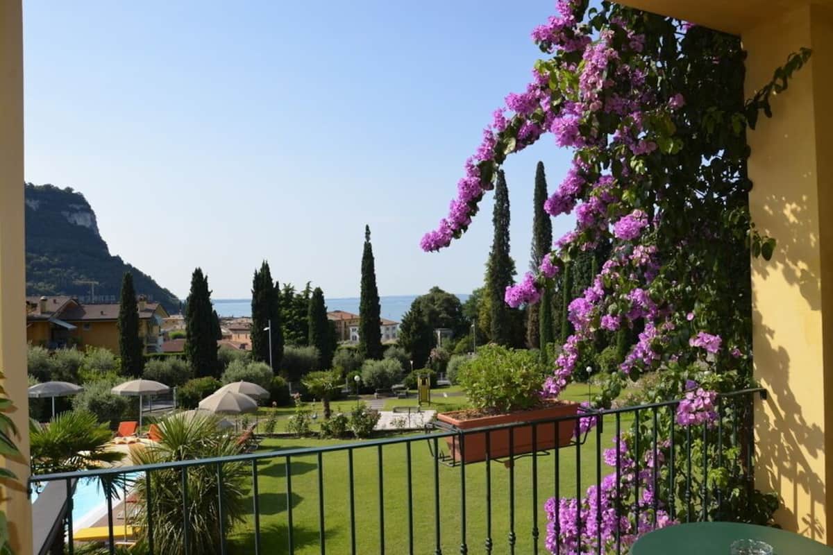 Un balcon donnant sur un jardin, une piscine et, au loin, une montagne.