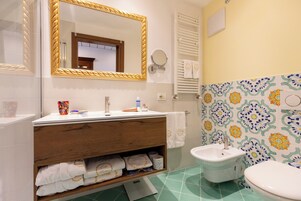 Un baño con tocador de madera, lavamanos, inodoro, espejo y baldosas estampadas.