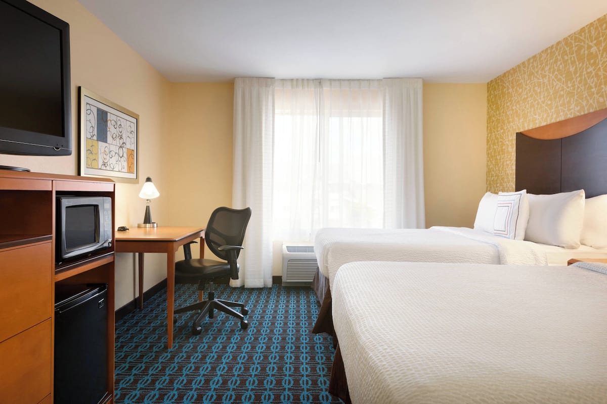 A hotel room with two beds, a desk with a chair, a television, and a small refrigerator.
