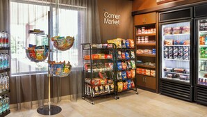 Un mercado de barrio con pasillos de aperitivos, secciones refrigeradas y vistas a través de un ventanal.