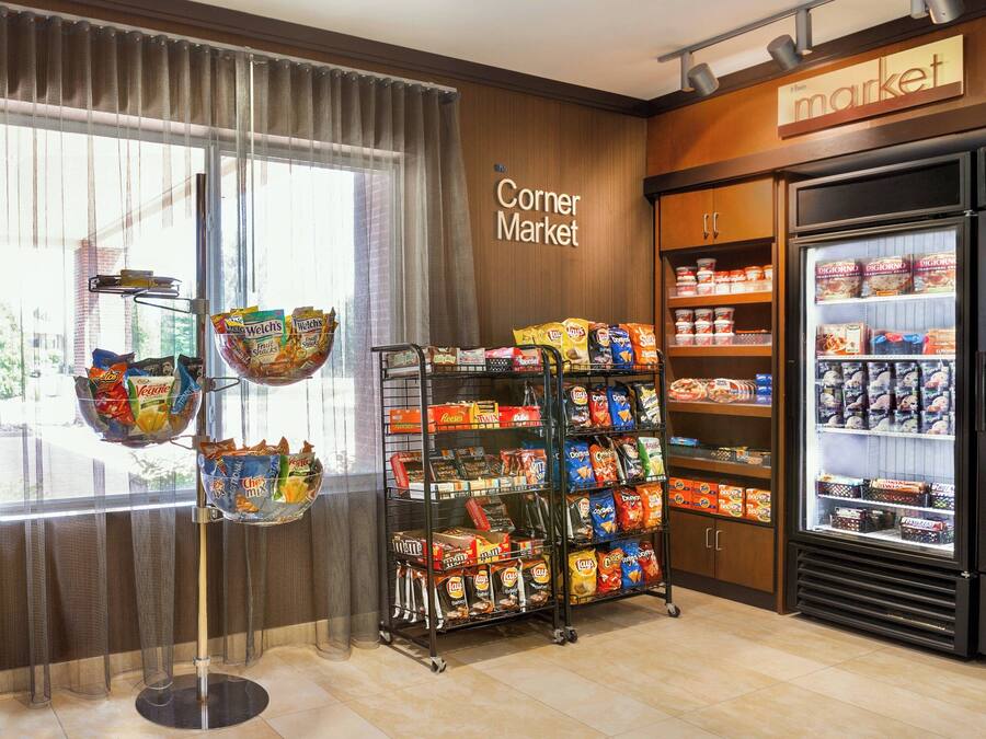 A corner market with snack aisles, refrigerated sections, and a view through a window.