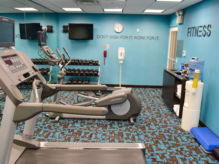 A fitness center with exercise equipment, a water dispenser, and motivational wall text.