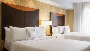 Habitación de hotel con dos camas, un cabecero grande, una lámpara y un ventanal con cortinas.