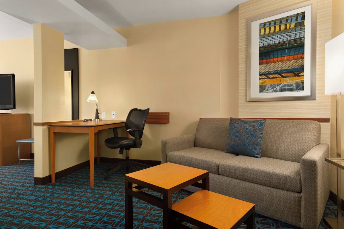 A hotel room with a sofa, a small table, a desk with a chair, a lamp, and a television.