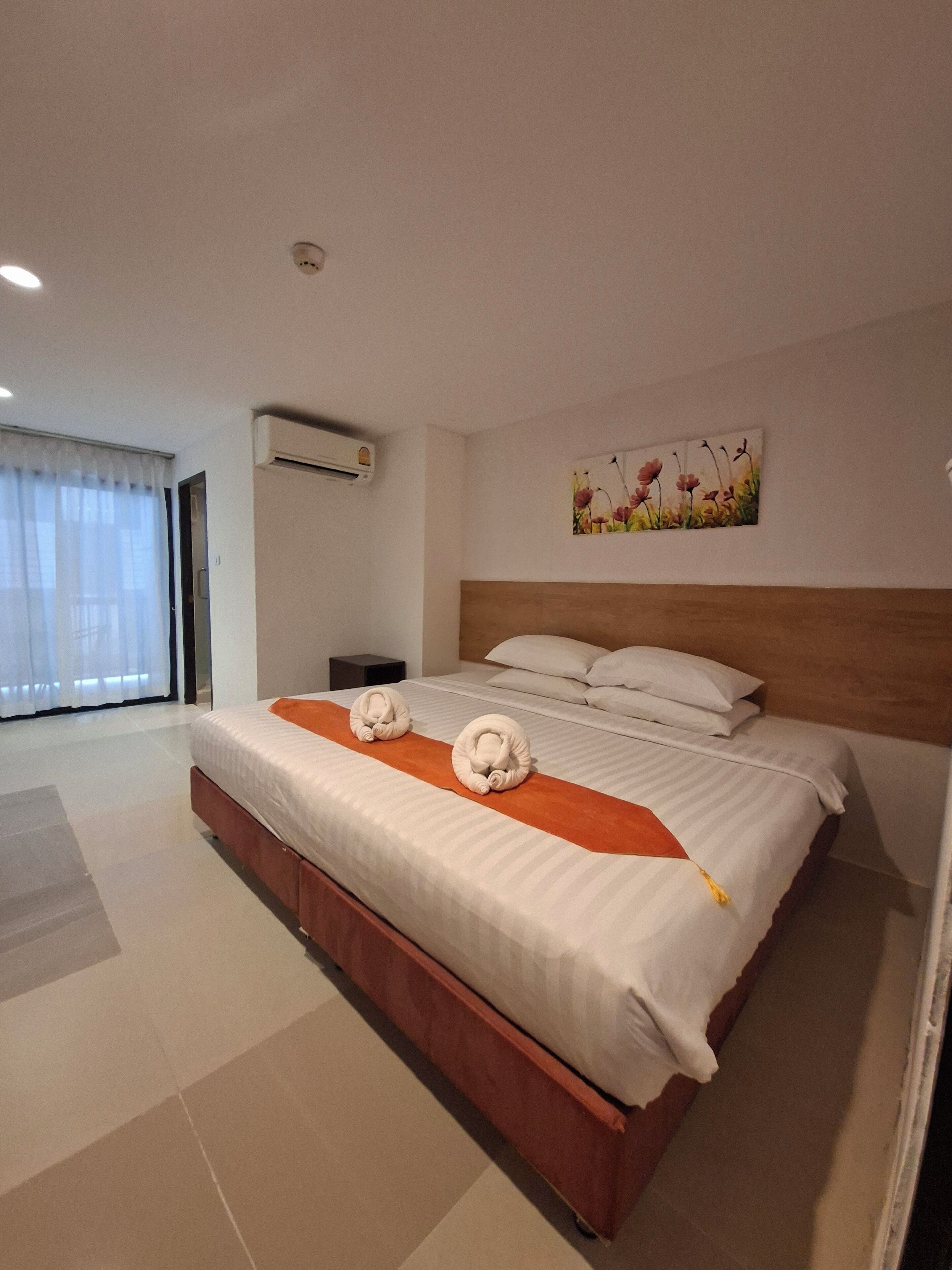 Habitación de hotel con una cama grande, cabecera de madera, un cuadro en la pared y un equipo de aire acondicionado.