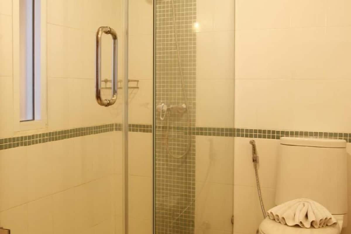 A shower with a glass door, a toilet, and a small window.