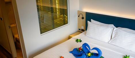 A hotel room with a neatly made bed, a bedside table with a lamp, and a window with blinds.