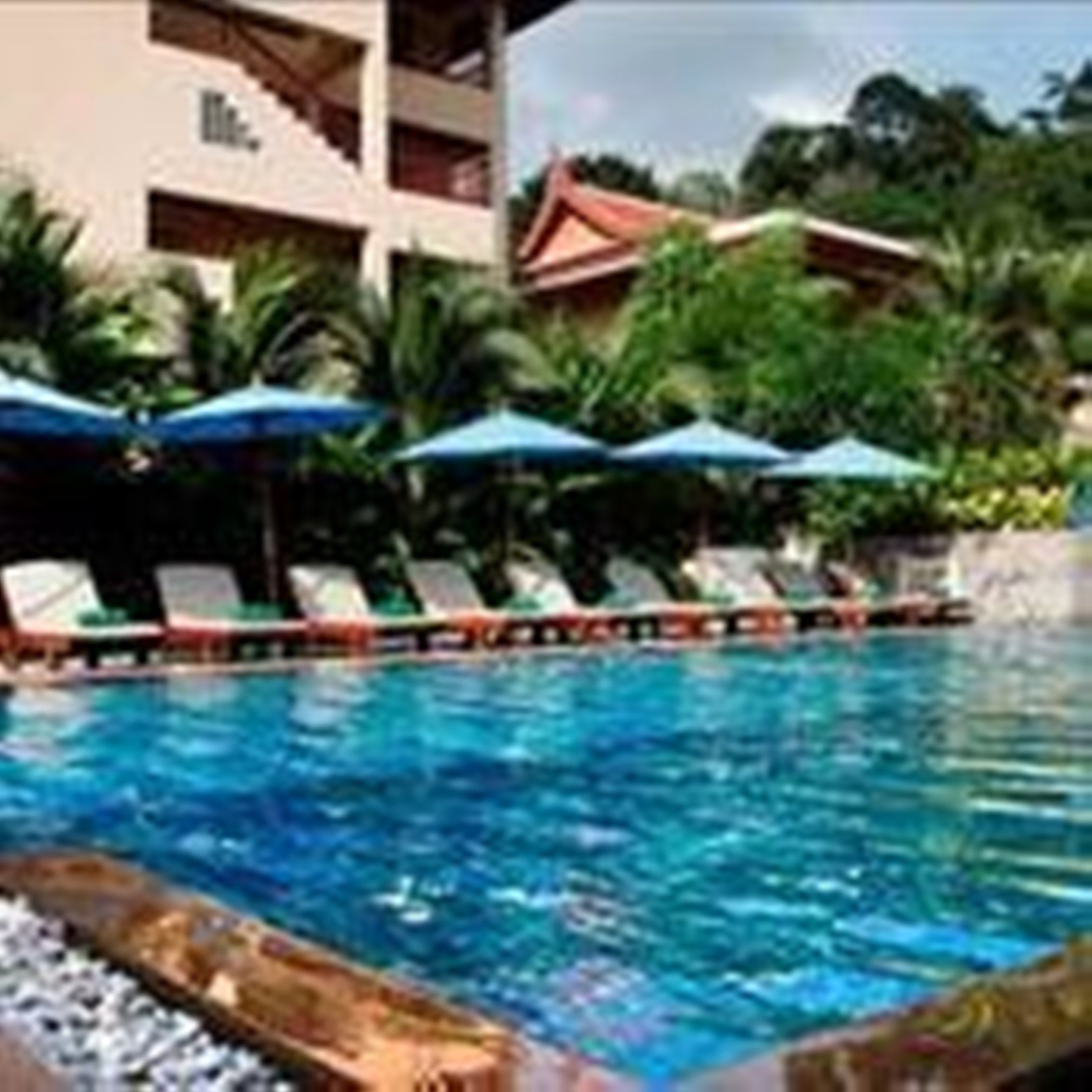A swimming pool with lounge chairs and umbrellas, surrounded by a building with a red roof and greenery.
