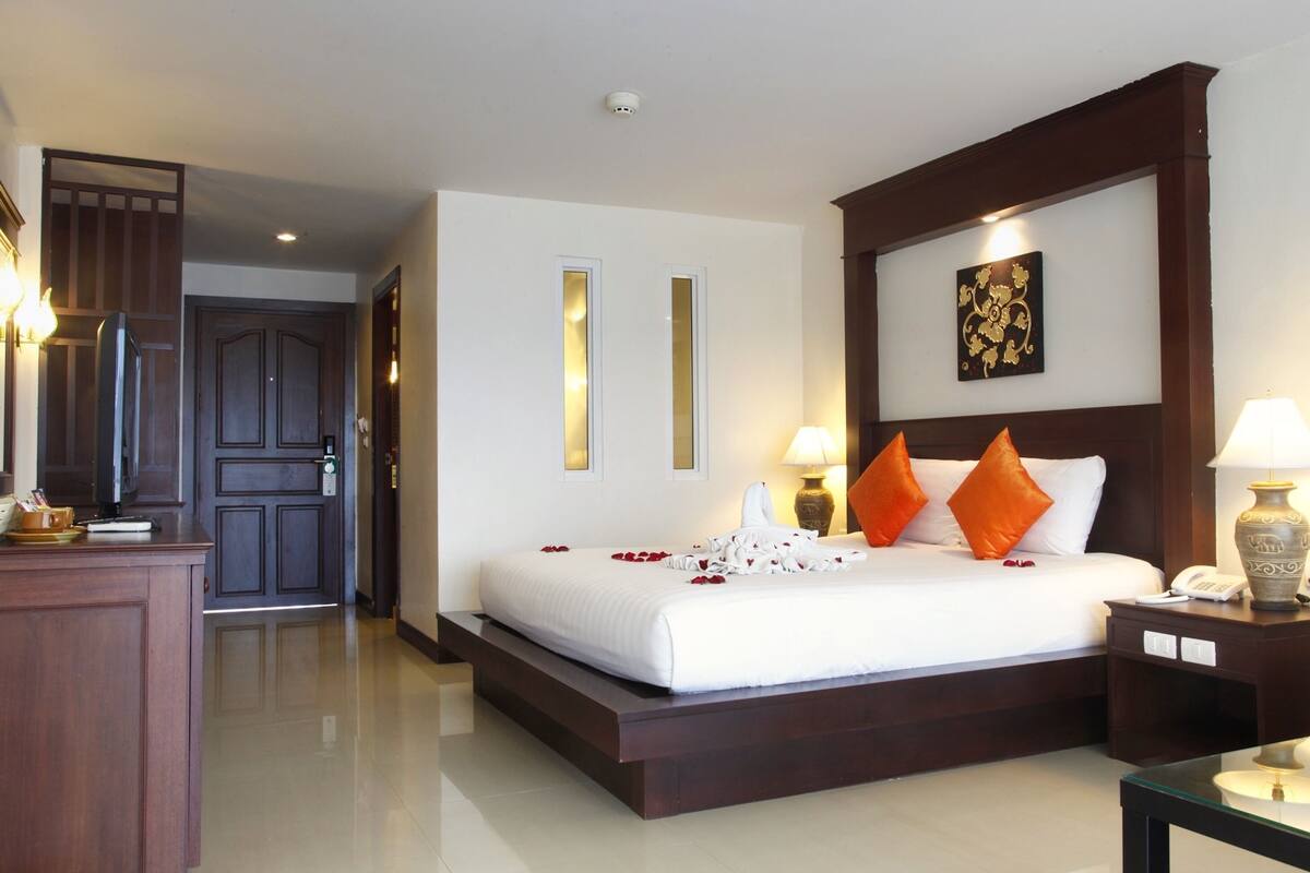 A hotel room with a large bed, two bedside lamps, a nightstand, a wooden headboard, and a decorative wall piece.