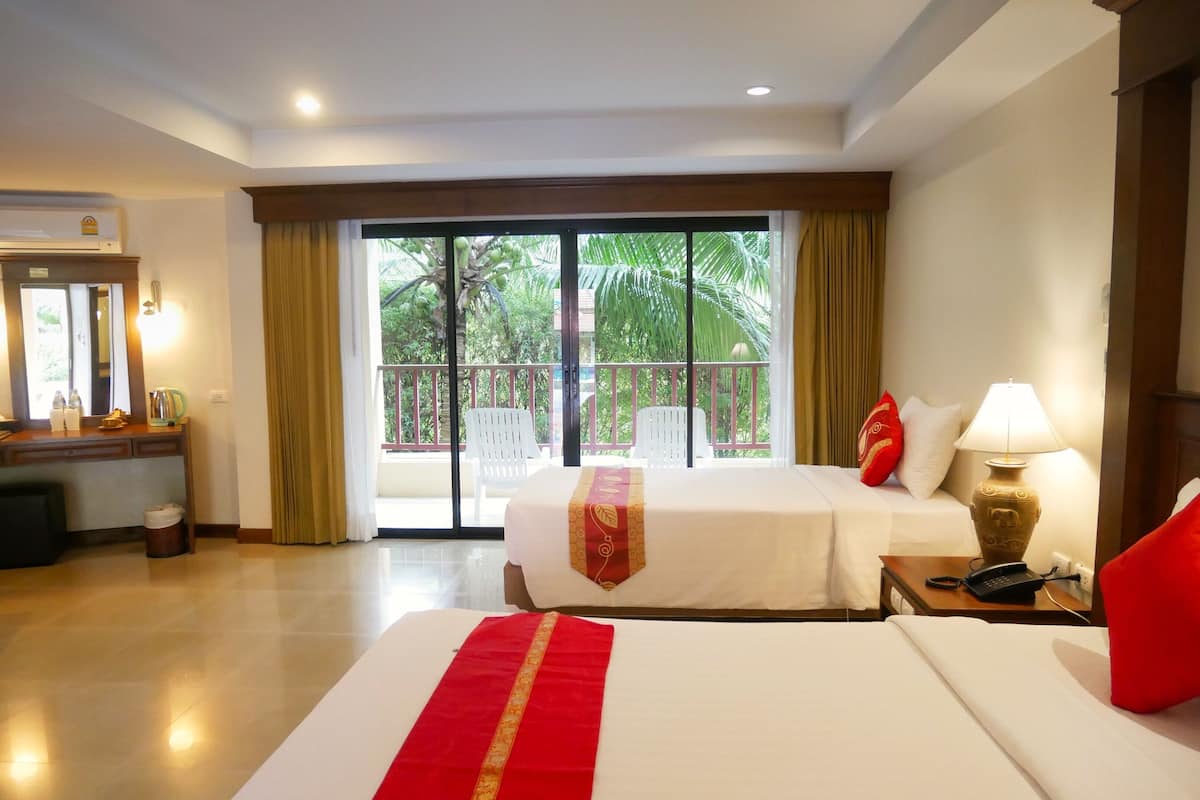 A hotel room with a large bed, a desk with a mirror, a chair, and a balcony with a view of palm trees.