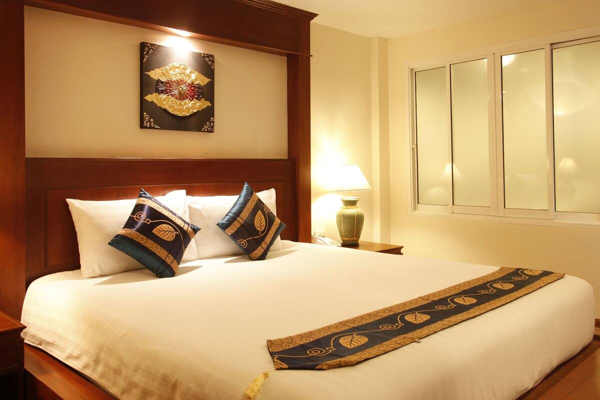A neatly made bed with a decorative headboard, a bedside lamp, and a window with frosted glass.