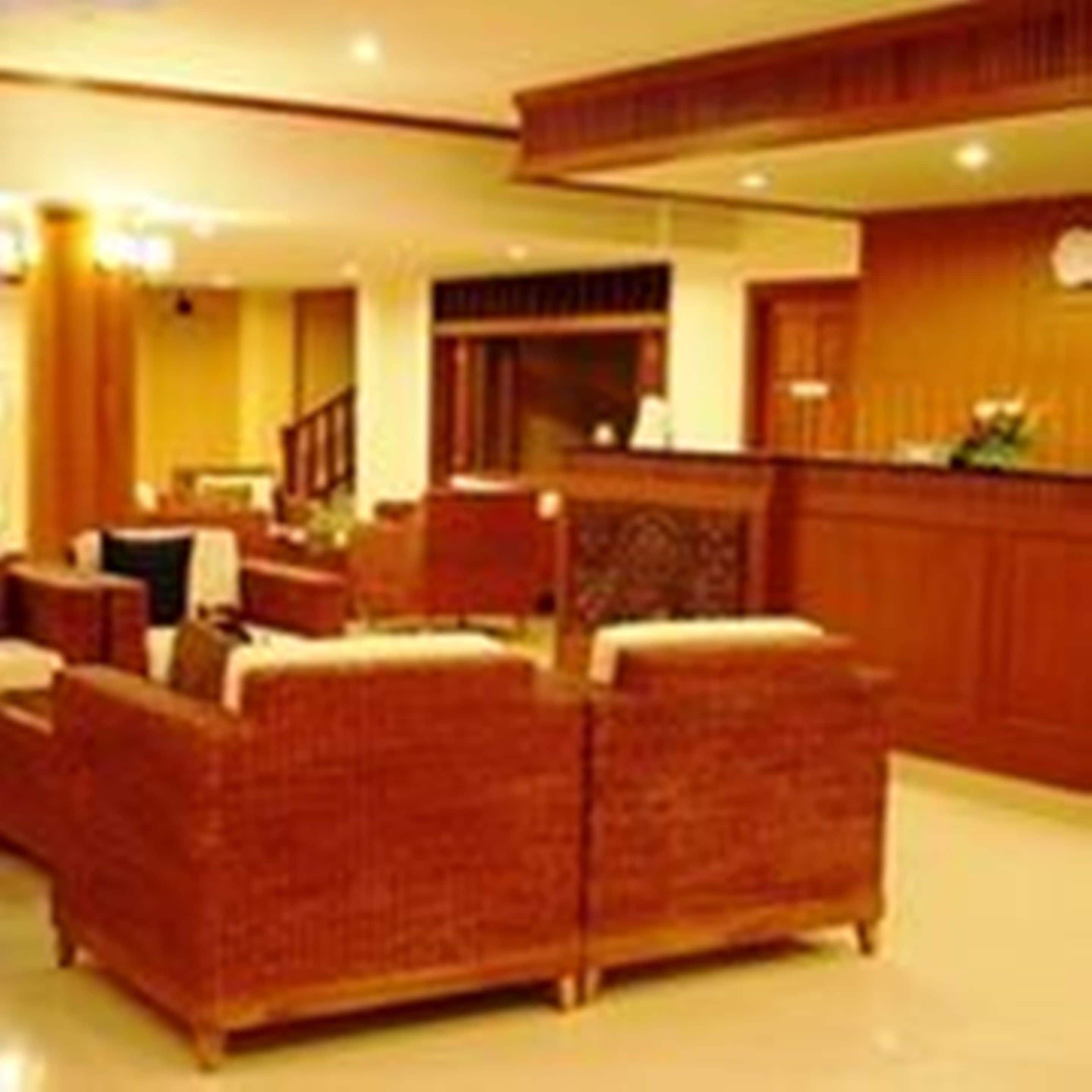 A hotel lobby with wicker furniture, a reception desk, and a staircase.