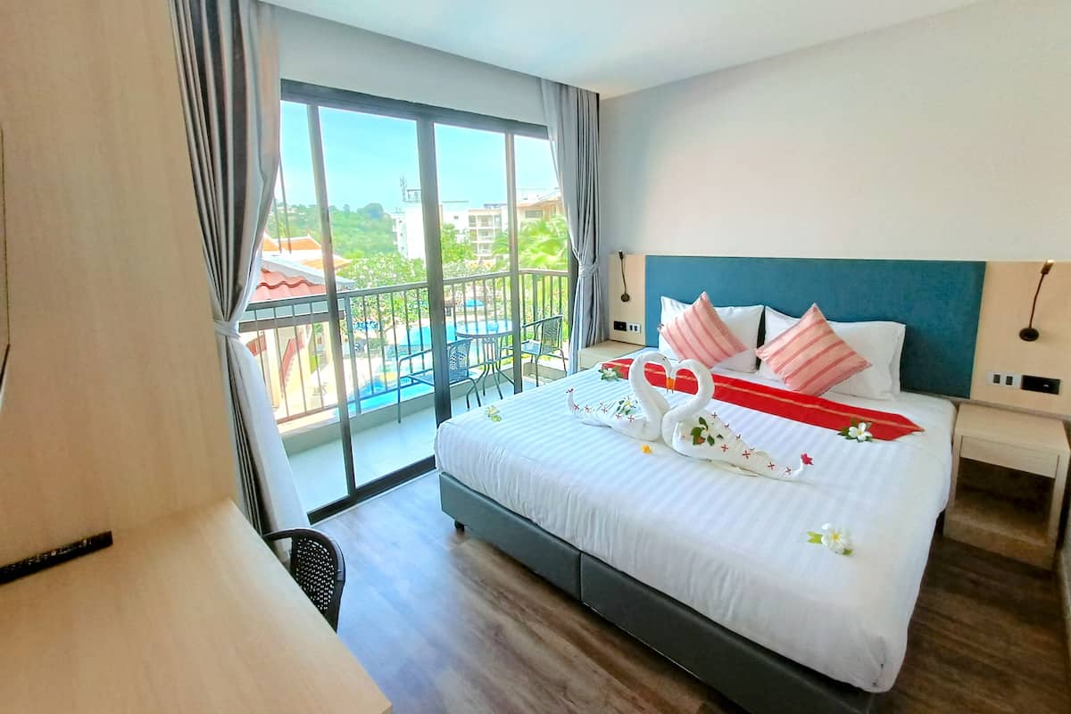 A hotel room with a large bed, a balcony with a view of the city, and a desk with a chair.