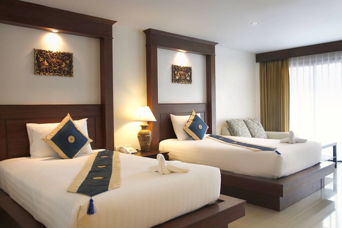 A hotel room with two beds, each with a headboard, bedside tables, lamps, and decorative wall art.