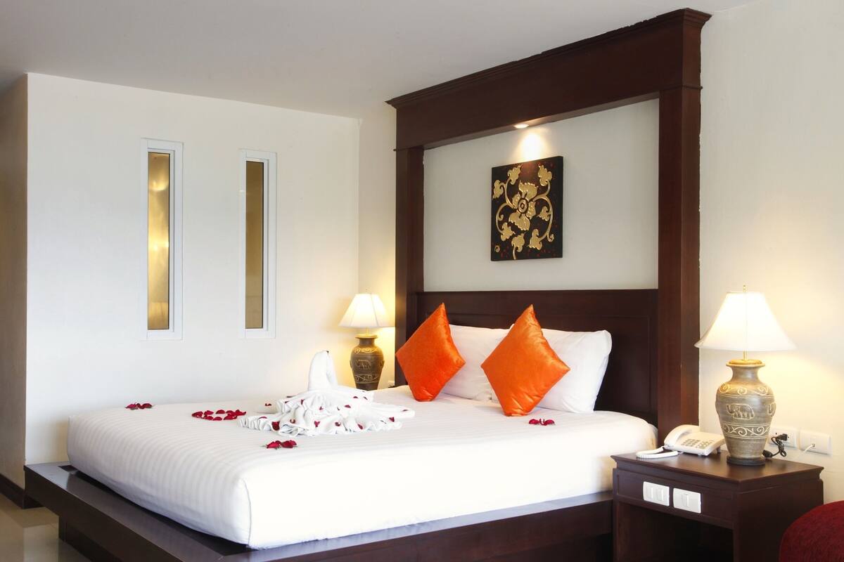 A neatly made bed with white linens, two orange pillows, and a decorative wall piece above it.
