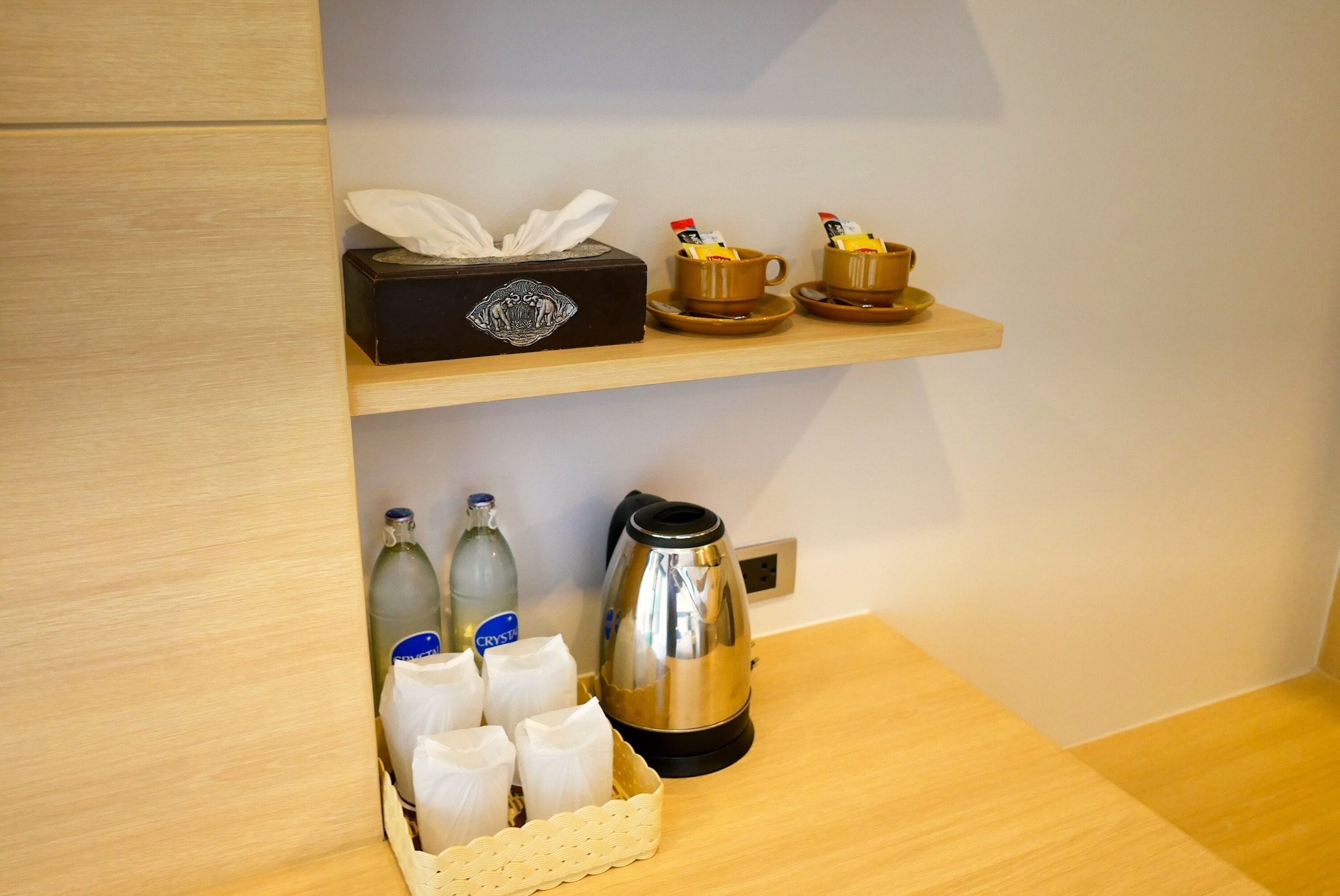 A wooden shelf with a tissue box, two cups with condiments, a kettle, and bottles.