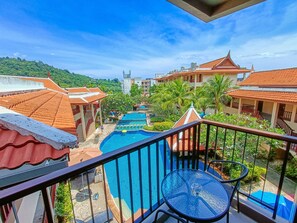 A balcony with a view of a swimming pool, palm trees, and traditional buildings. - Baan Yuree Resort and Spa (Patong)