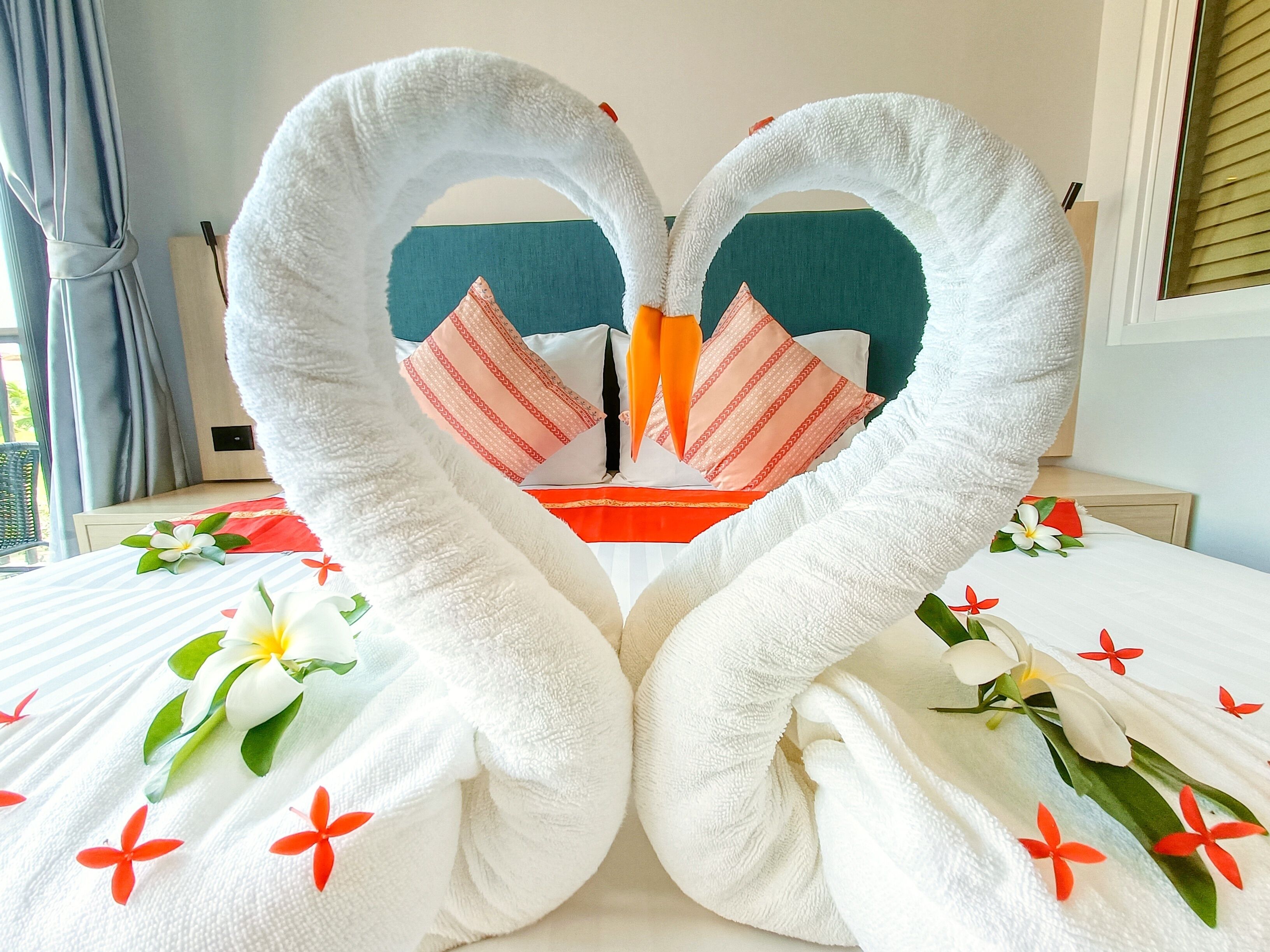 A bed with a heart-shaped towel arrangement, a pillow with a striped pattern, and a floral bedspread.