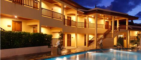 Un hotel de varios pisos con piscina, balcones y una zona exterior cubierta.