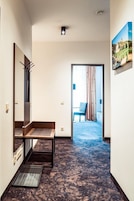 A hotel hallway with a bench, a mirror, and a door leading to a room with a bed and curtains.