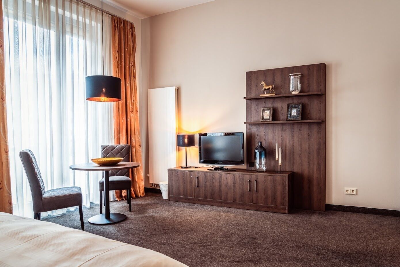 Habitación de hotel con cama, televisión, escritorio con silla, lámpara y aparador con adornos.