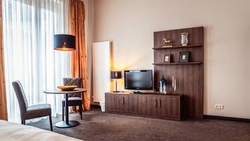 Habitación de hotel con cama, televisión, escritorio con silla, lámpara y aparador con adornos.