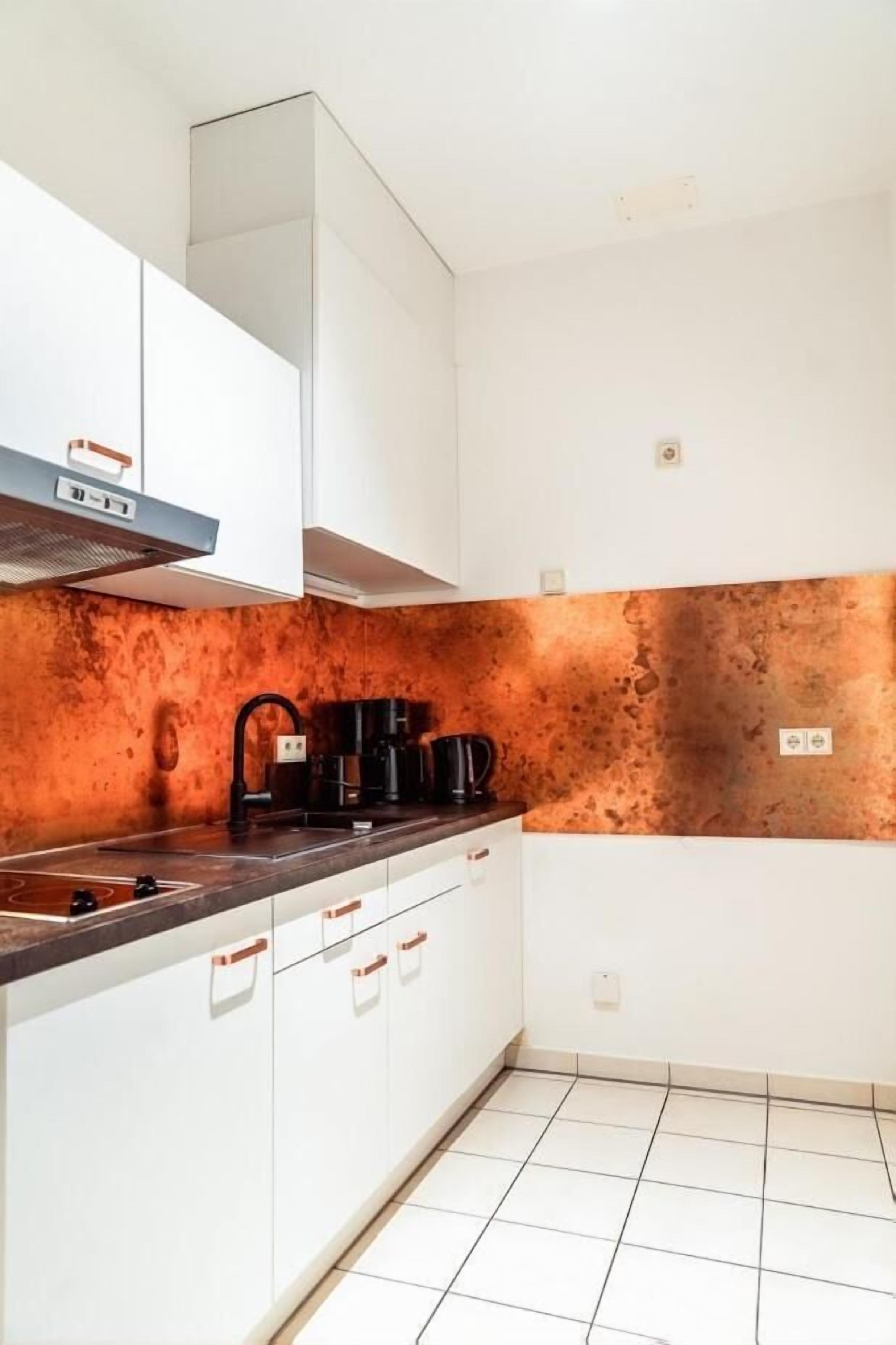 A kitchen with white cabinets, a copper backsplash, and a black coffee maker.