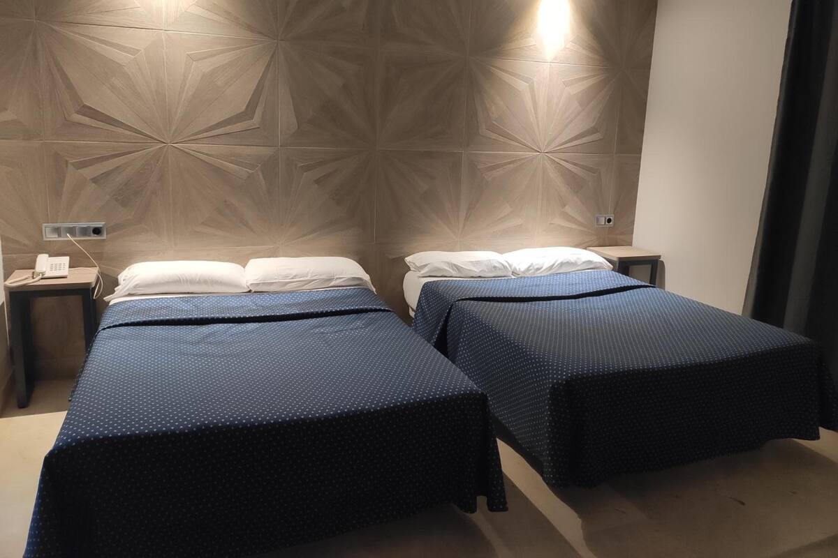 Habitación de hotel con dos camas, un teléfono en la mesita de noche y una pared con diseño geométrico.