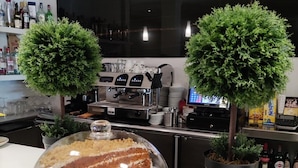 Un coin cuisine avec un gâteau exposé dans une vitrine, deux plantes en pot et une machine à café.