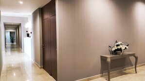 Un couloir avec une porte en bois sombre, un comptoir d’accueil et un vase de fleurs posé sur une console.
