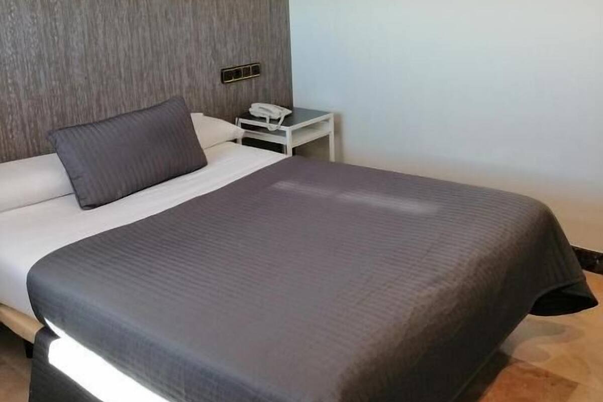 Una habitación de hotel moderna con una cama grande, una mesita de noche y un cabecero de madera.
