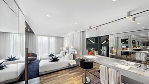 A modern hotel room with a large bed, a sitting area, a vanity with a mirror, and a view of the hotel's interior. - W London (London)