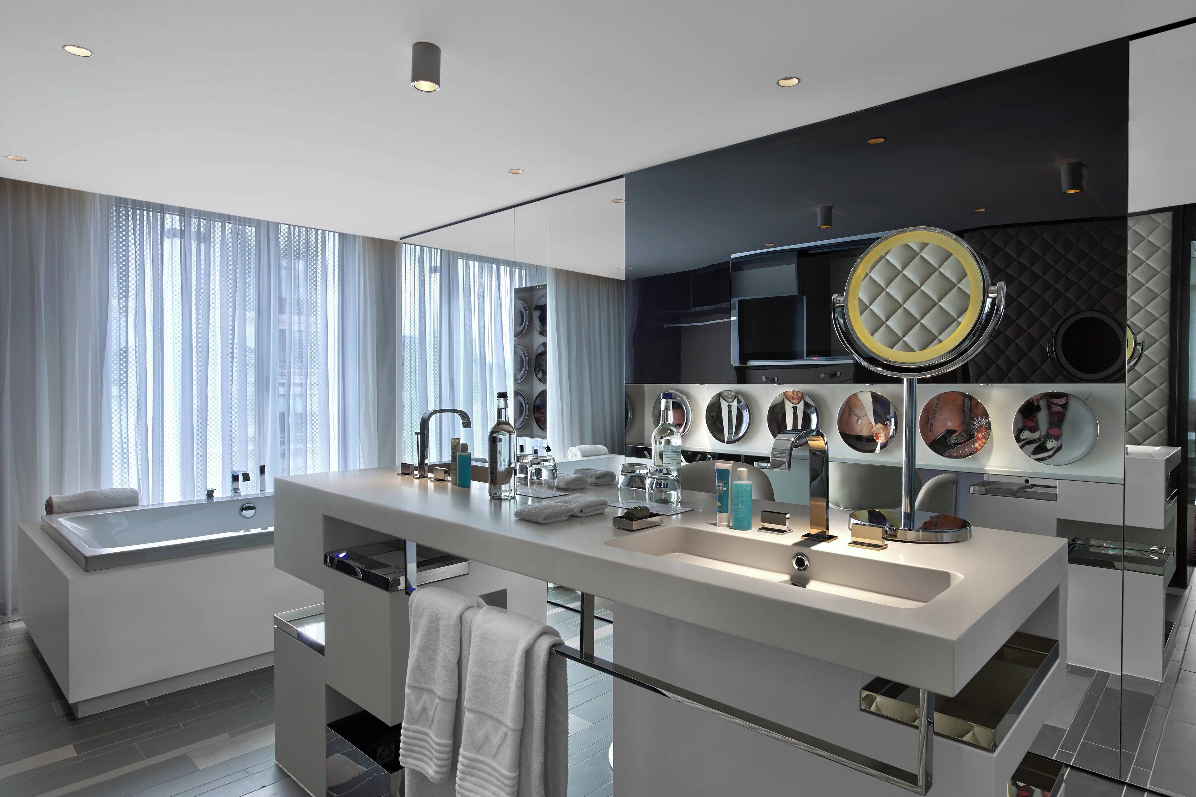 Un baño moderno con una bañera grande, un tocador con espejo y un ventanal con cortinas de gasa.